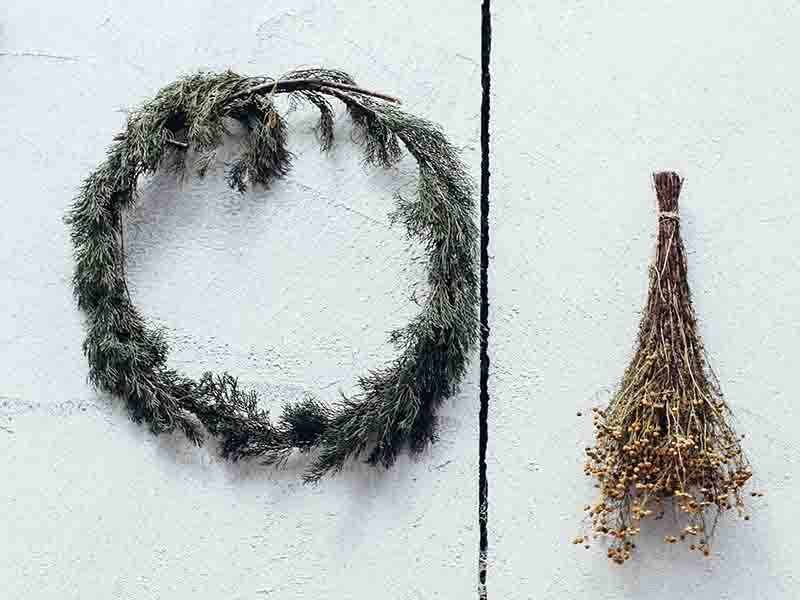 Wreath and bundled dried flowers hanging on white wall