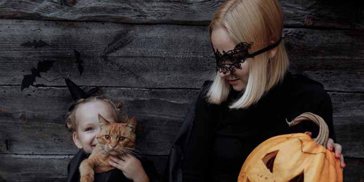 Mother and daughter in matching halloween costumes, holding a jackolantern
