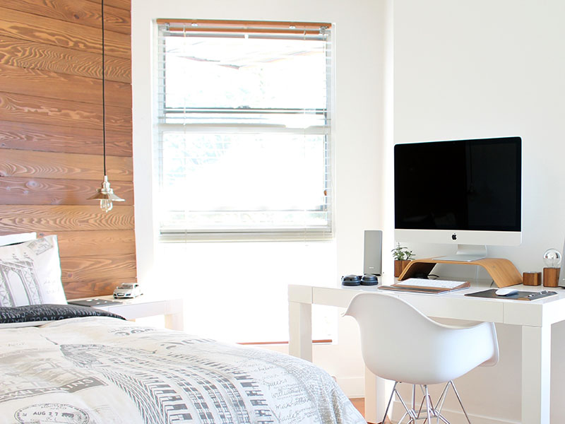 Clean bedroom with white walls, a white desk, and large white computer monitor.