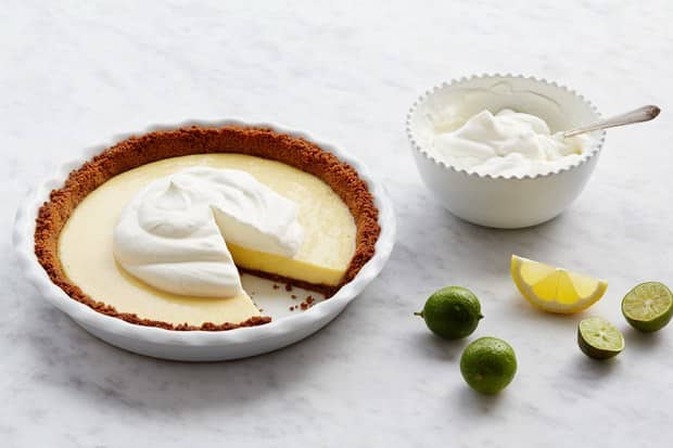 Key lime pie on a table with limes and whipped cream