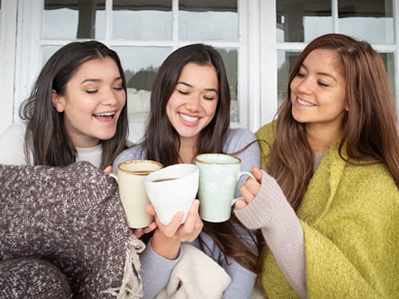 three friends holding mugs wrapped in blankets