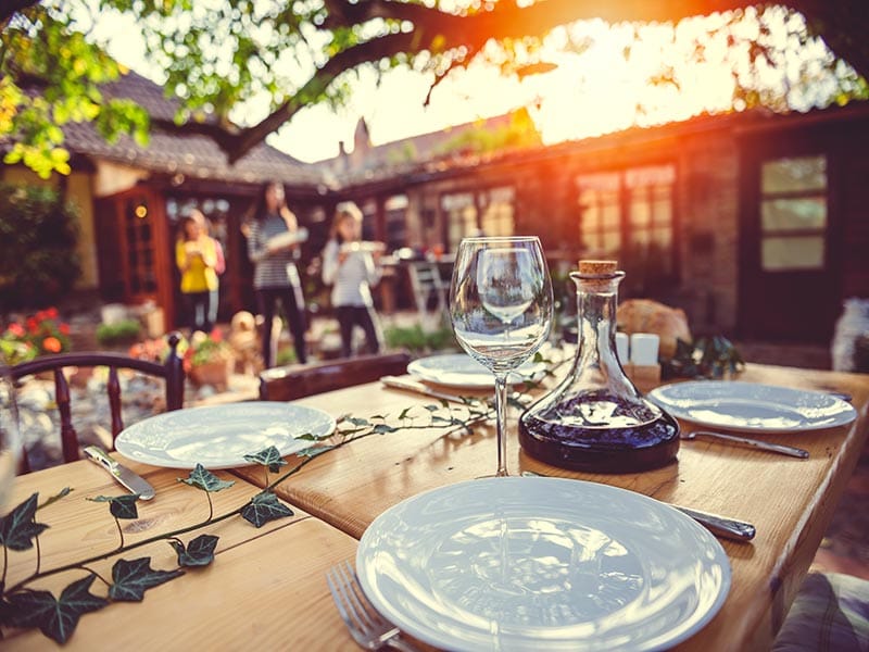 Table set for meal outside at sunset, people and home in the background