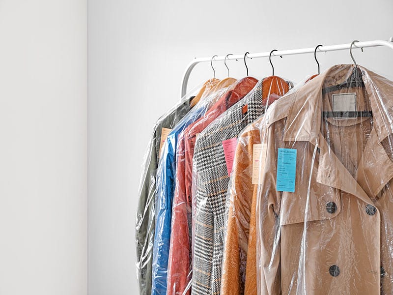 clothes wrapped in dry cleaning bags hanging on rack