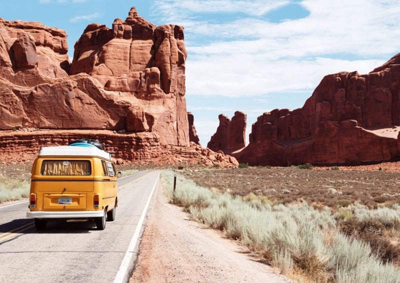 VW van driving amidst red rock formations