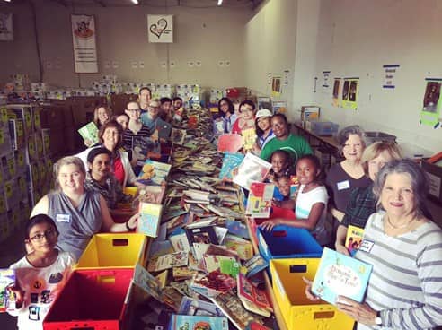 children and adults gathered around a long table with tons of books