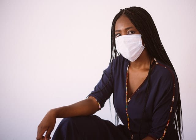 black woman with long hair wearing face mask posed in front of white wall