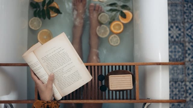 bath tub filled with sliced citrus and leaves with a shelf and open book