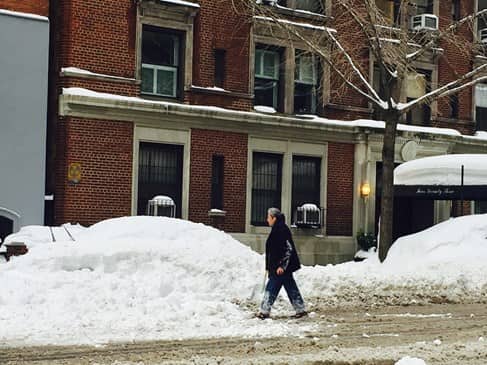 Older woman walking by cars that are covered by snow in NYC