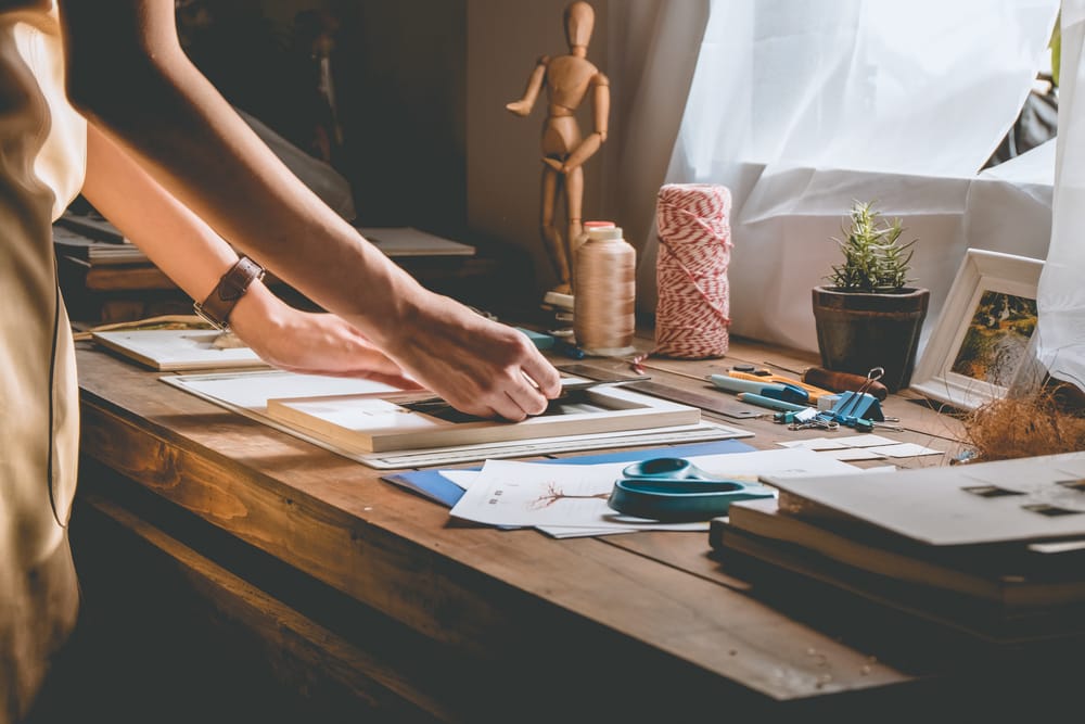 Woman hand crafting book at a table with stationery.