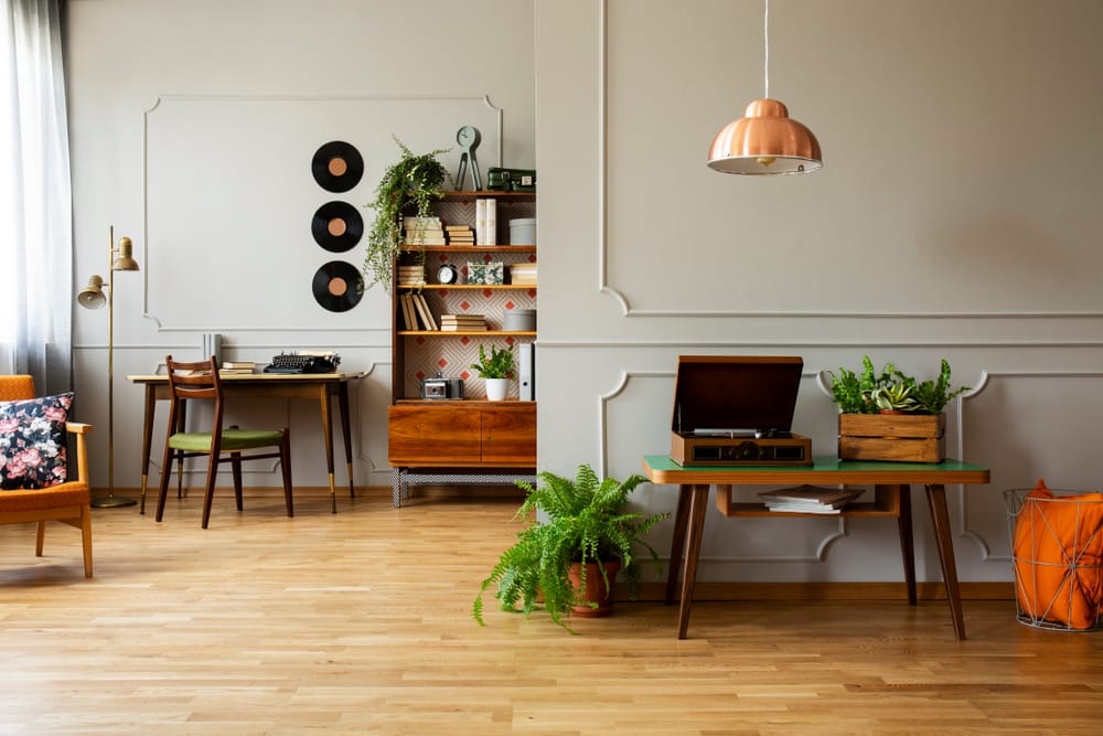 Record player and plant on wooden table in grey apartment interior with lamp and vinyl