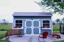 Blue garden shed with white trim in a rock garden