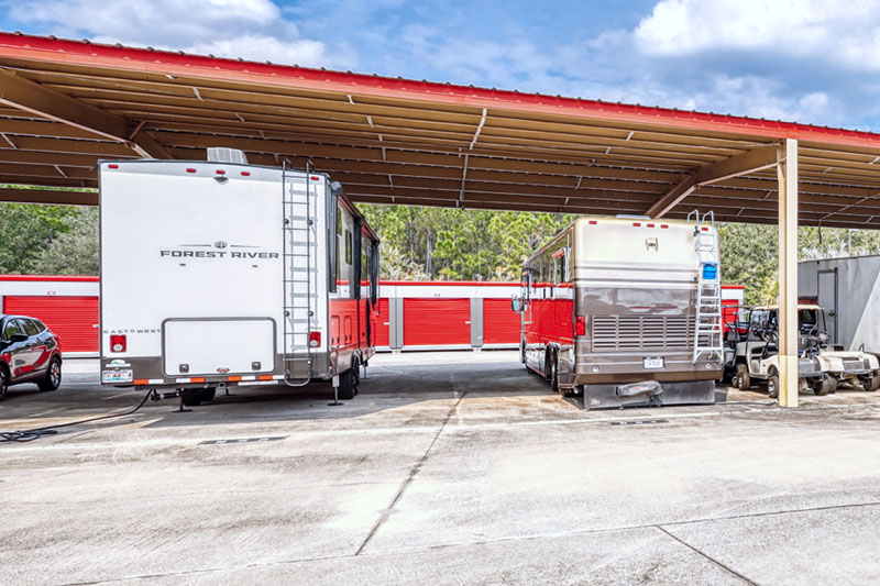 Parked RVs under a metal canopy in a storage parking lot.