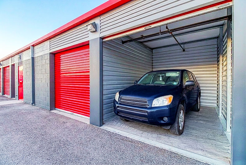 A blue car inside a wide drive up storage unit.