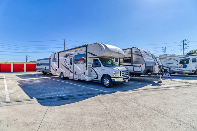 Parked RVs and trailers outside with storage doors in the distance.